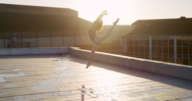 Ballet dancer performing an elegant jump on a rooftop at sunset, showcasing grace and flexibility. Ideal for promoting dance studios, fitness and wellness centers, or illustrating concepts of freedom and art. Suitable for use in magazines, blog posts, and social media campaigns emphasizing beauty and strength.