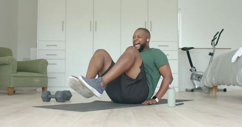 Man performing core workout on mat in bright bedroom with dumbbells and water bottle