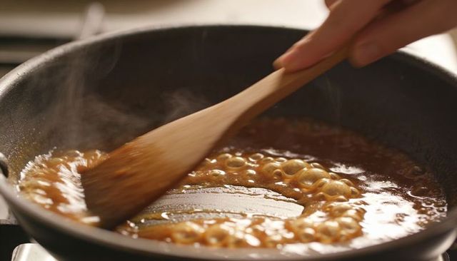 Stirring glossy caramel sauce in nonstick pan with wooden spatula, bubbling steam