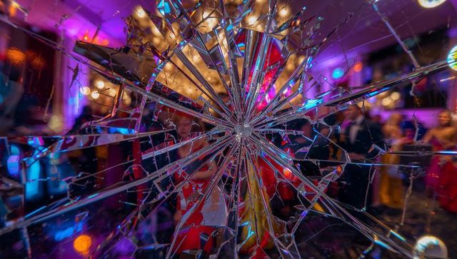 Shattered glass reflecting colorful gala lights and elegant guests in prismatic ballroom
