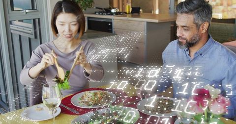 Midadult asian woman serving salad to partner with ar overlay at modern kitchen table