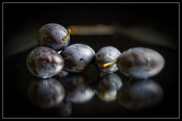 Cluster of plump, fresh purple grapes resting on shiny mirrored surface. Ideal for use in food blogs, healthy eating promotions, organic produce marketing, and culinary visuals. Highlights the natural beauty and richness of fresh fruit, suitable for health and wellness related content.