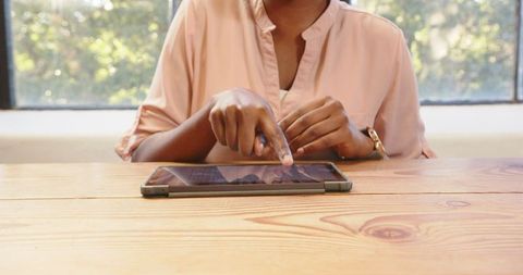 African American Woman Using Tablet at Wooden Desk Focusing on Work
