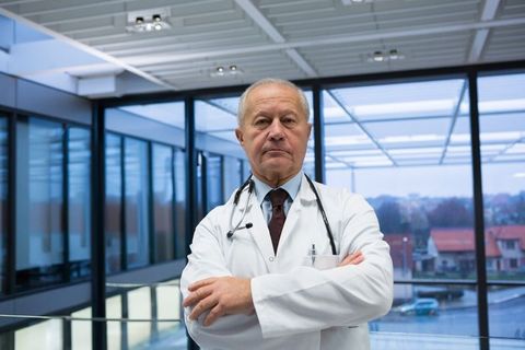 Confident Senior Doctor in Hospital Corridor With Crossed Arms