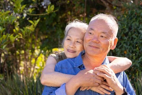 Asian senior couple embracing in sunlit garden, enjoying peaceful outdoor romance and companionship