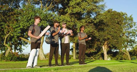 Cricket players standing on crease clapping and cheering on sunny grass field