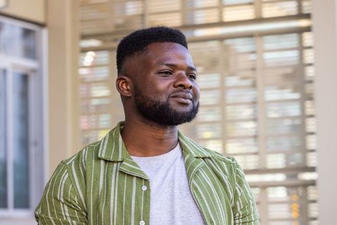 Confident African man looking right standing by window blinds wearing green striped shirt