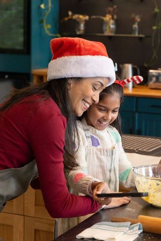 Indian mother and daughter mixing batter in cozy holiday kitchen wearing santa hats