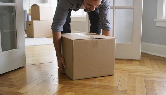 Man lifting large cardboard box on parquet floor during home move, unpacking and organizing