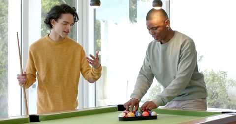 Multiracial male friends racking pool balls in bright home game room casual leisure social