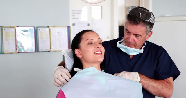 A middle-aged Caucasian dentist is examining a young Caucasian woman's teeth, with copy space. His professional demeanor and her relaxed posture suggest a routine dental check-up in a well-equipped clinic.