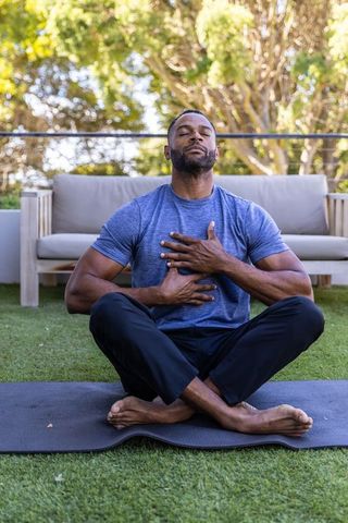 African american man practicing mindful breathing meditation on backyard yoga mat