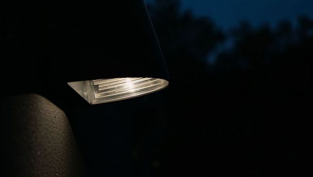 Warm Wall Sconce Casting Soft Glow on Textured Stucco at Night with Ribbed Diffuser Modern Fixture