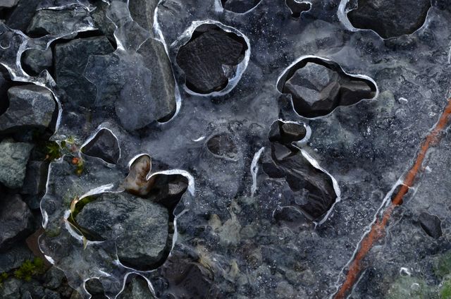 Close-up view of rocks encased in ice, showing natural texture and pattern. Suitable for use in backgrounds, environmental themes, nature-related content, and abstract art projects illustrating winter or cold environments.