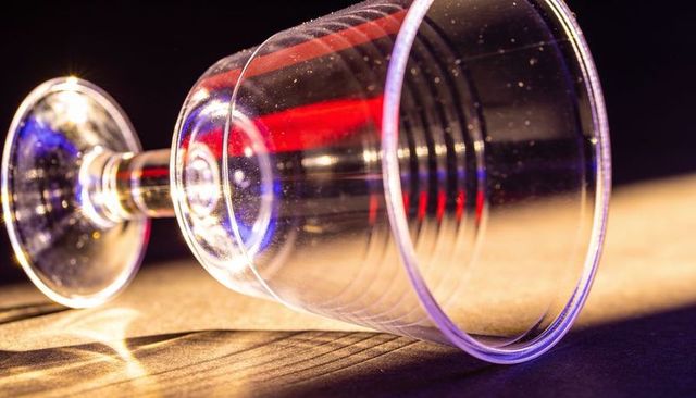 Tipping clear plastic wine glass reflecting colored lights and casting dramatic shadows