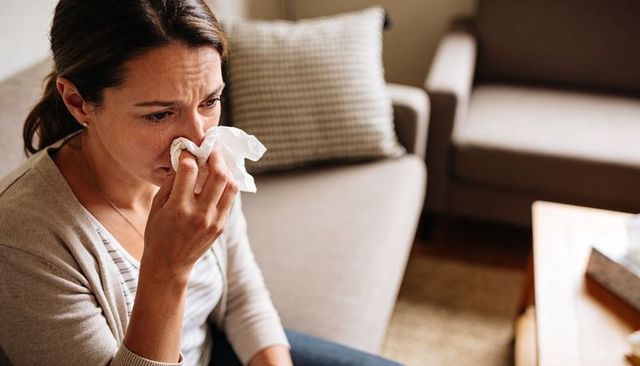 Crying woman wiping nose on couch experiencing grief and solitude in cozy living room