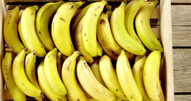 Collection of fresh yellow bananas arranged attractively in a wooden crate, placed on a rustic wooden surface. Great for healthy living articles, advertisements for organic produce, vibrant social media posts, and websites focusing on nutritious food.