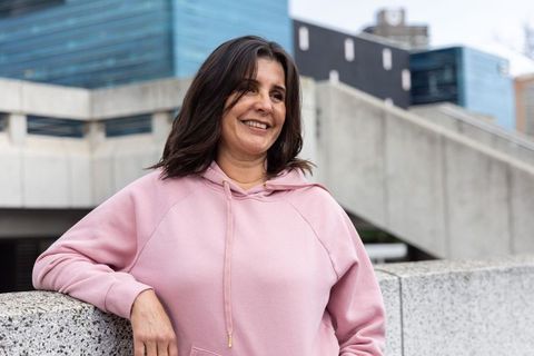 Smiling woman leaning on urban rooftop parapet wearing pastel pink hoodie casual city portrait