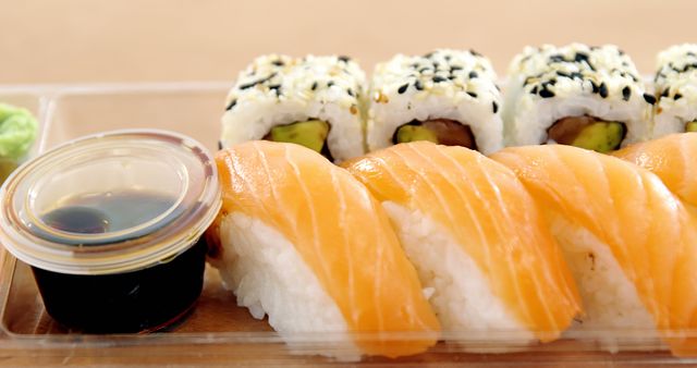 A tray of sushi features a variety of rolls and sashimi, including avocado rolls sprinkled with sesame seeds and slices of fresh salmon over rice, accompanied by soy sauce and wasabi. Sushi is a traditional Japanese dish enjoyed worldwide for its fresh flavors and artistic presentation.