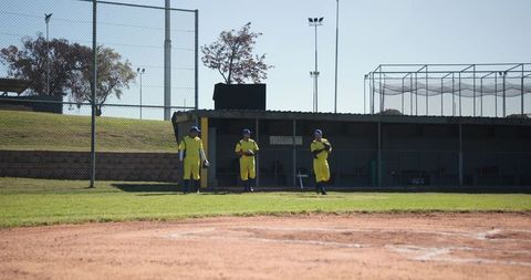 Baseball teammates walking toward dugout in yellow uniforms on sunny ballfield
