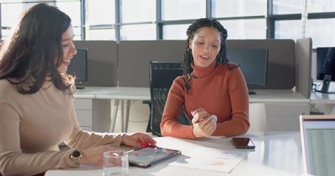 Female Colleagues Collaborating Over Tablet and Analytics Charts in Bright Modern Office