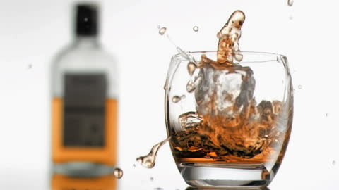 Whiskey Splashing in Glass with Bottle in Background