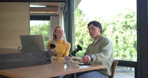 Co-hosts recording home podcast with laptop microphones and headset, collaborative workspace