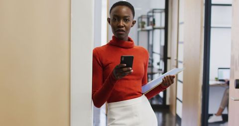 Businesswoman using smartphone in modern office hallway