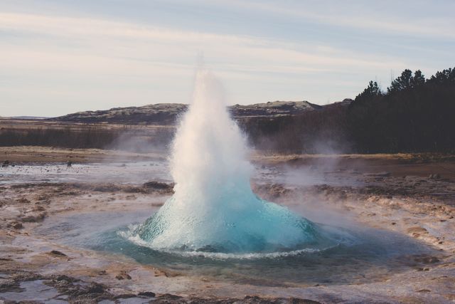 Captures a geyser in mid-eruption, surrounded by a rocky landscape and clear skies. Ideal for use in travel blogs, educational materials about geothermal activity, nature scenery collections, environmental studies, or promoting natural wonders and attractions.