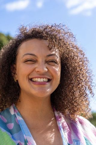 Smiling african american woman with curly hair and pastel scarf, joyful outdoor portrait