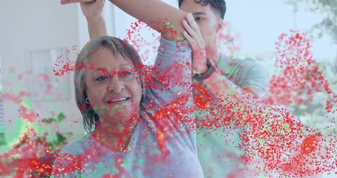 Caregiver guiding senior stretching arm in bright home therapy with colorful particles
