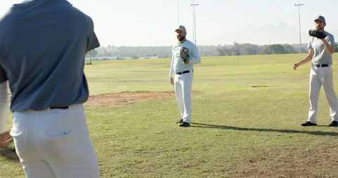 Sunlit baseball teammates warming up on grassy field holding gloves and wearing caps
