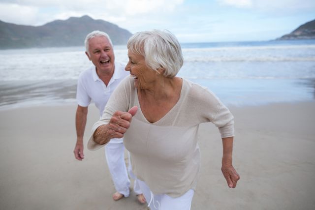 Senior couple enjoying a playful moment on the beach, showcasing happiness and togetherness. Ideal for use in advertisements promoting retirement plans, senior lifestyle products, travel agencies, and health and wellness campaigns. Highlights the joy and freedom of retirement and active living.