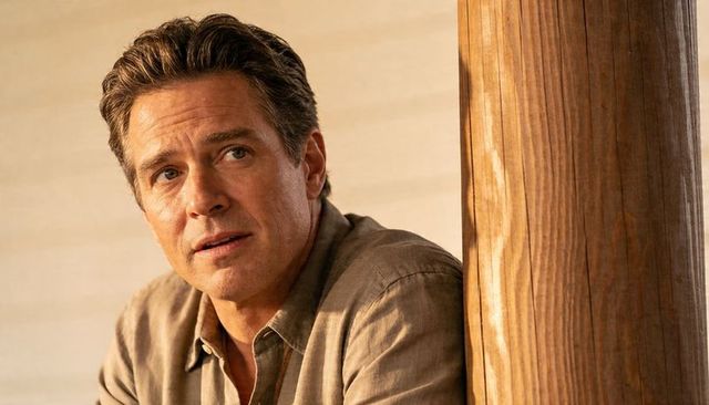 Contemplative man leaning on wooden post gazing left in warm golden light portrait closeup