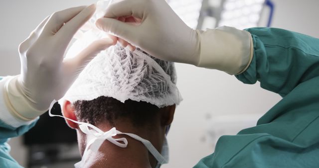 Healthcare worker is putting on protective cap and gloves, preparing for a surgical procedure. Ideal for medical, healthcare, or hospital themed content showcasing professionalism, hygiene, and patient care protocols in medical settings.