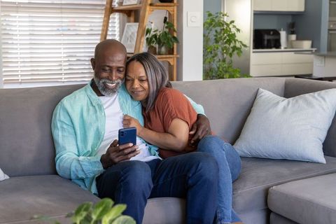 African american couple relaxing on sofa sharing smartphone moments