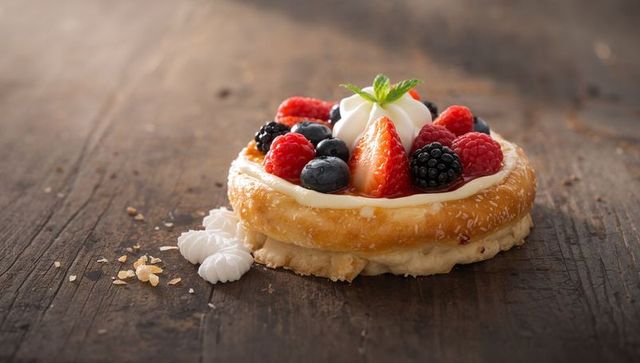 Glazed berry ring tart with vanilla custard, whipped cream and mint on rustic wood