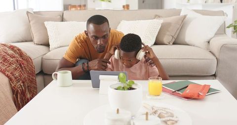 Father guiding son with tablet and headphones, mentoring during relaxed home learning