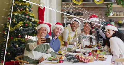 Friends taking selfie at festive holiday dinner wearing santa hats sharing warm laughter
