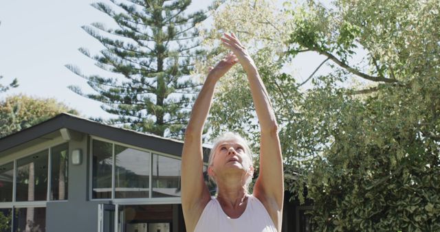 Focused senior caucasian woman wearing sports clothes and raising hands in garden. Retirement, activity and senior lifestyle, unaltered.