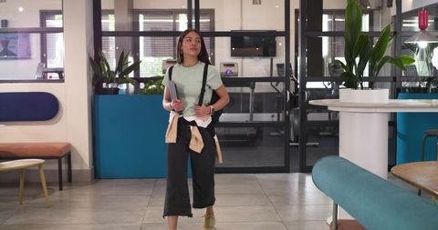 African american woman walking through coworking lounge carrying notebooks backpack