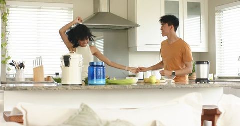 Young couple dancing and holding hands in bright modern kitchen with granite countertop