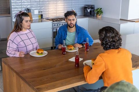 Diverse friends sitting around wooden kitchen island sharing burgers and red sodas