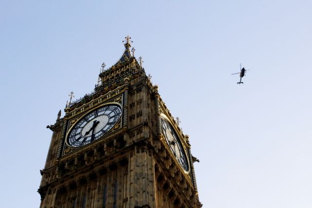 Big Ben clock tower in London with helicopter flying in clear sky. Iconic British landmark perfect for travel-related advertisements, educational content about British landmarks, or articles highlighting London's most famous attractions.