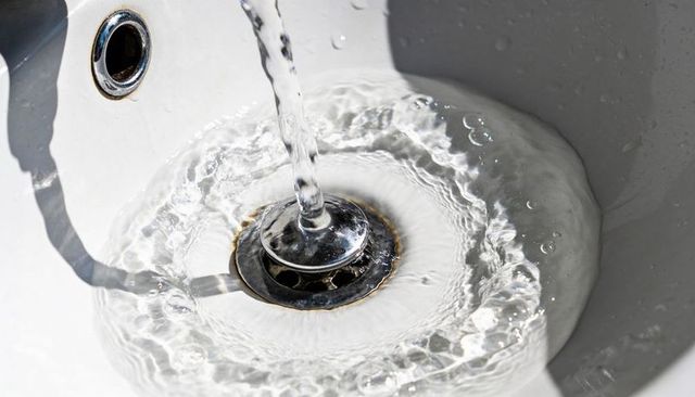 Clear water swirling around chrome drain in white porcelain bathroom sink with ripples