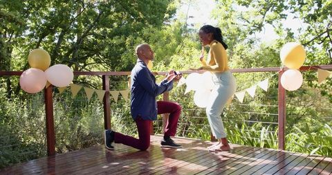 Romantic proposal on deck with balloons in sunny outdoor setting