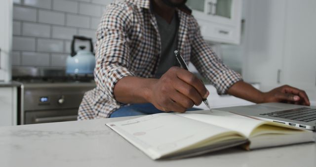 Man Taking Notes While Working On Laptop In Kitchen - Download Free Stock Images Pikwizard.com