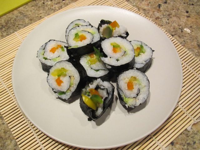 Freshly made vegetarian sushi rolls filled with various vegetables arranged on a white plate, placed on a sushi mat. Ideal for use in food blogs, healthy eating articles, cooking tutorials, Japanese cuisine promotions, and vegetarian diet recipes.