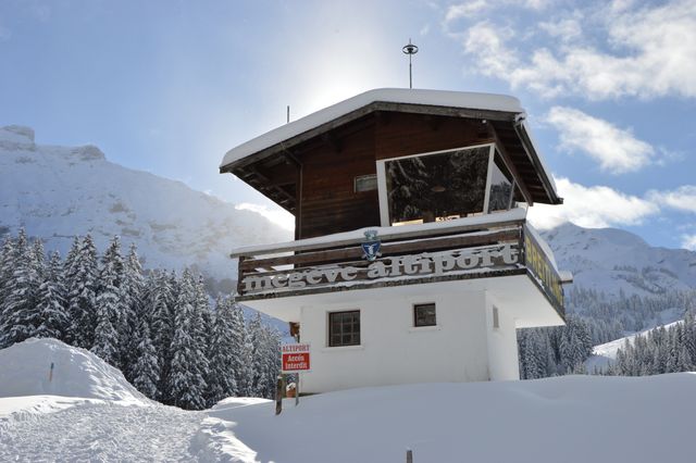 Beautiful snow-covered mountain chalet with bright sunlight shining through. Ideal for use in travel brochures, winter holiday promotions, tourism advertisements, and alpine region showcases. Highlights the serene and picturesque landscape, perfect for winter sports enthusiasts and nature lovers.