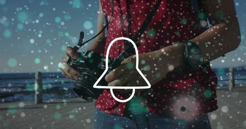 Holding dslr on seaside promenade adjusting lens while wearing red polka dot top and wristwatch